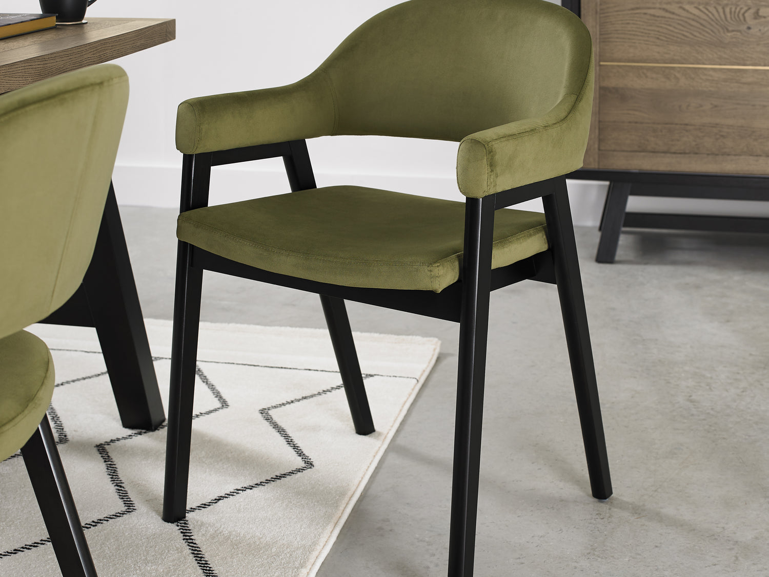 Angled image of the Candice Velvet dining chairs with curved back, armrests, and dark legs.