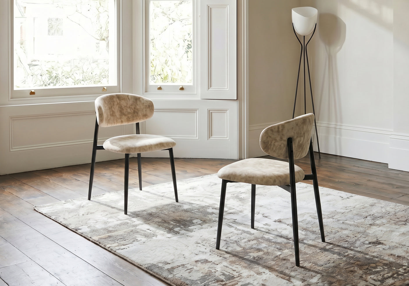 Two beige chairs with black legs in a room with large windows and a lamp.