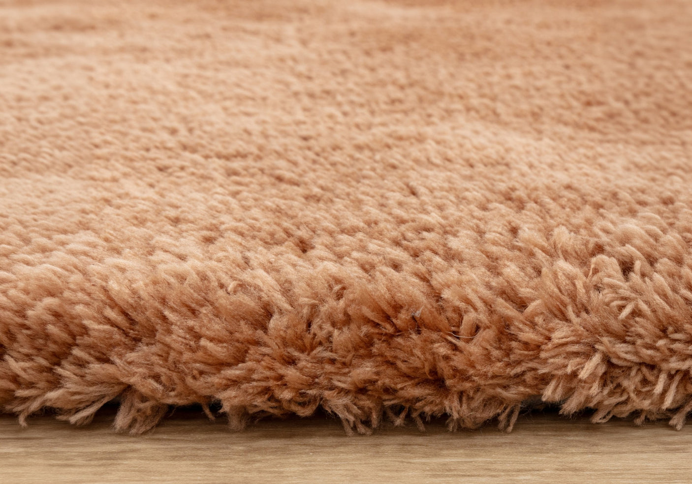 A close up of a terracotta rug on a wood floor.