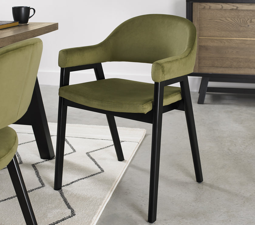 Angled image of the Candice Velvet dining chairs with curved back, armrests, and dark legs.