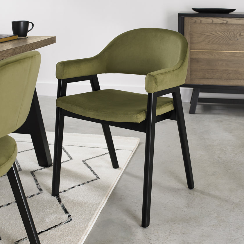 Angled image of the Candice Velvet dining chairs with curved back, armrests, and dark legs.