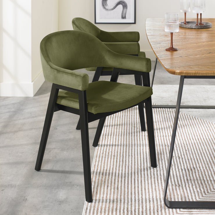 Angled image of the Candice Velvet dining chairs with curved back, armrests, and dark legs.