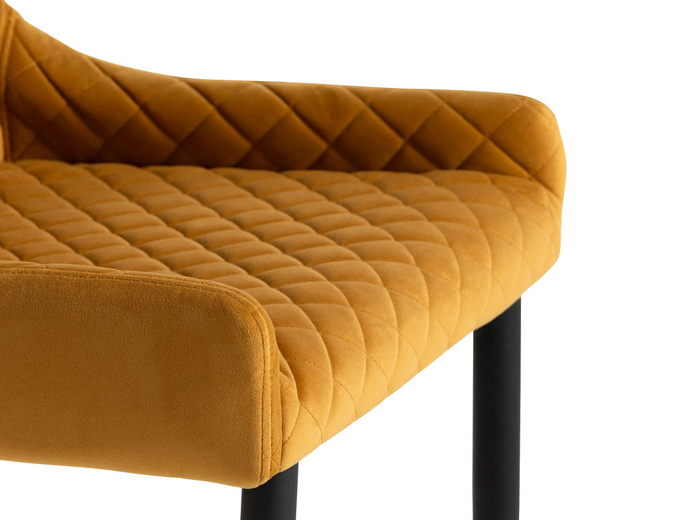 Mustard yellow quilted chair with black legs on a white background