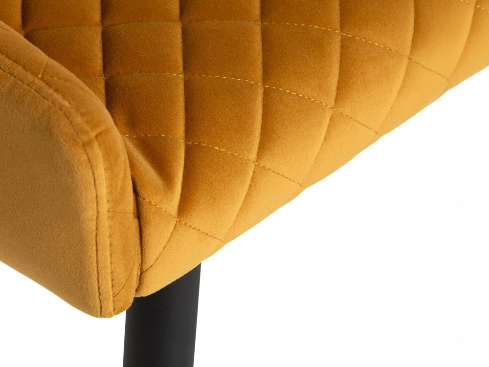 Close-up of a mustard yellow quilted chair with a black leg on a white background
