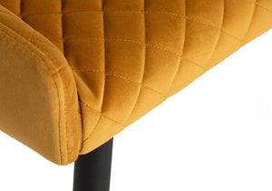 Close-up of a mustard yellow quilted chair with a black leg on a white background