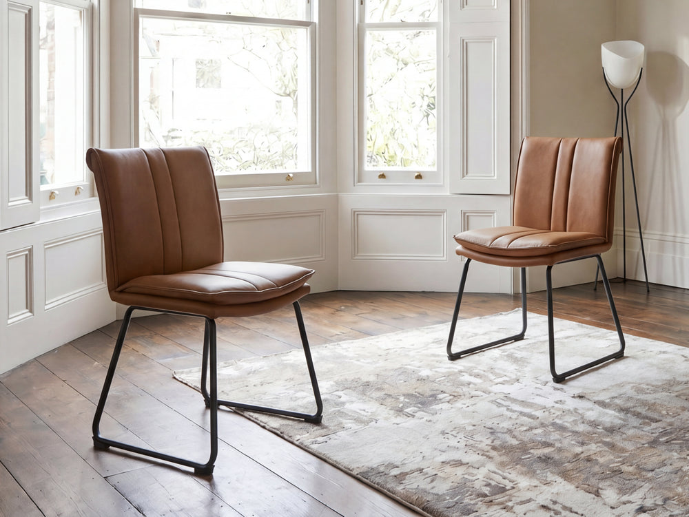 Two brown leather chairs in a room with large victorian windows and a rug.