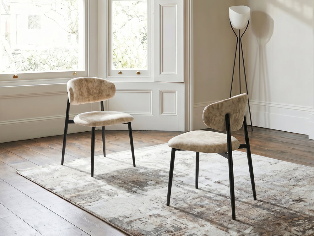 Two beige chairs with black legs in a room with large windows and a lamp.