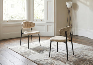 Two beige chairs with black legs in a room with large windows and a lamp.