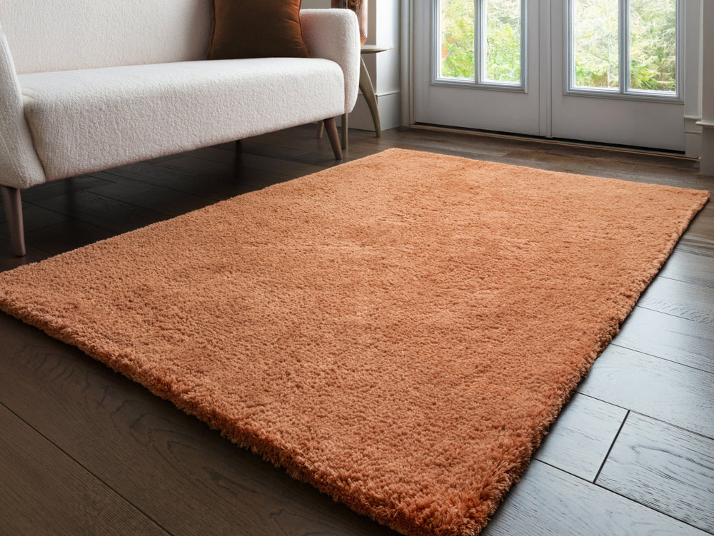A terracotta rug on a wooden floor with a sofa in the background.
