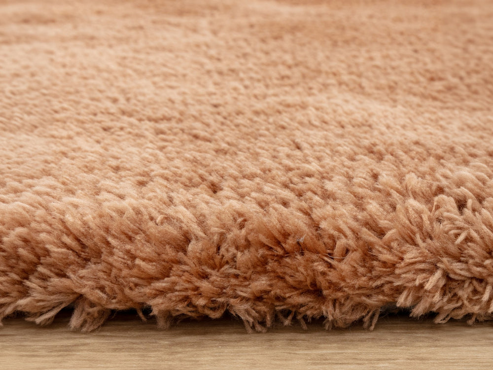 A close up of a terracotta rug on a wood floor.