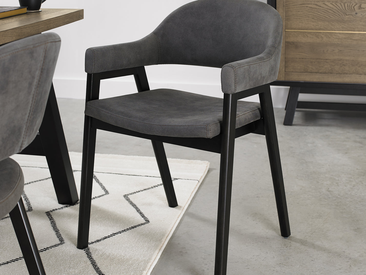 Angled view of the Candice Dark Grey Fabric Dining Chairs with Armrests and Oak Frame.