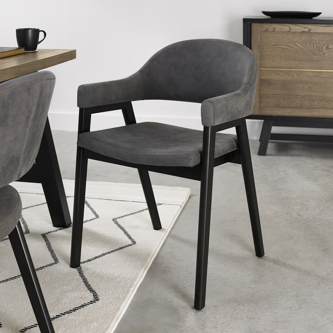 Angled view of the Candice Dark Grey Fabric Dining Chairs with Armrests and Oak Frame.