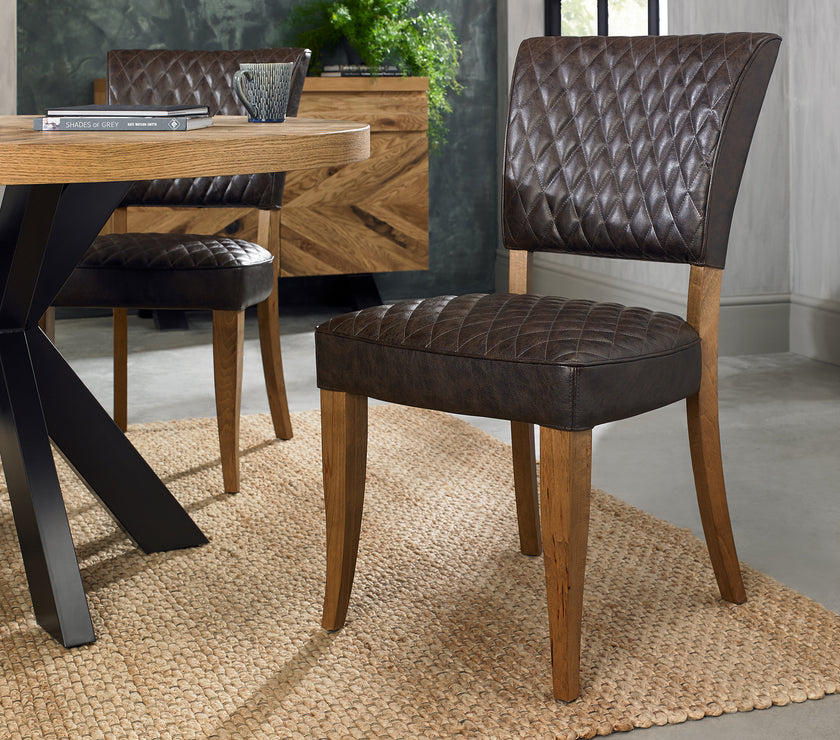 Angled image of the Landon Rustic Oak Dining Chairs with lightly oiled oak frame and saddle brown faux leather seat.