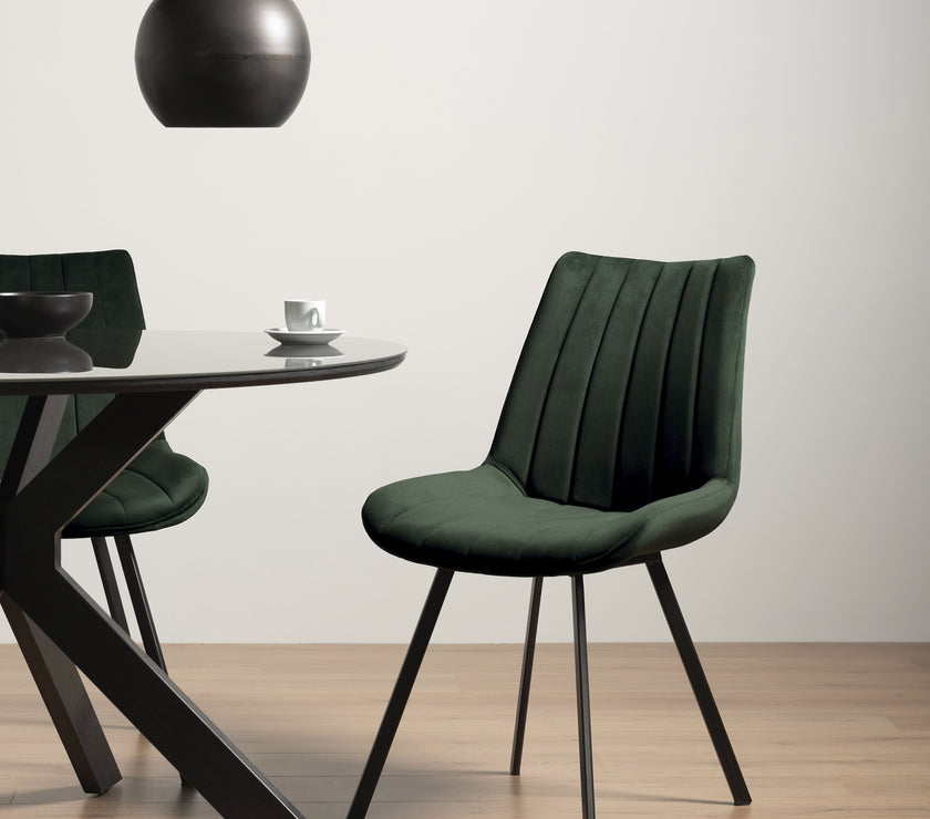 Long distance view of the Savio Dining Chairs in green velvet with vertical stitching and metal legs.